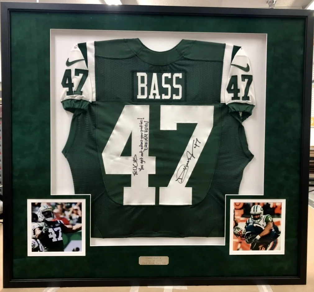 Autographed Jets jersey in a black shadow box with a green suede mat and action photos