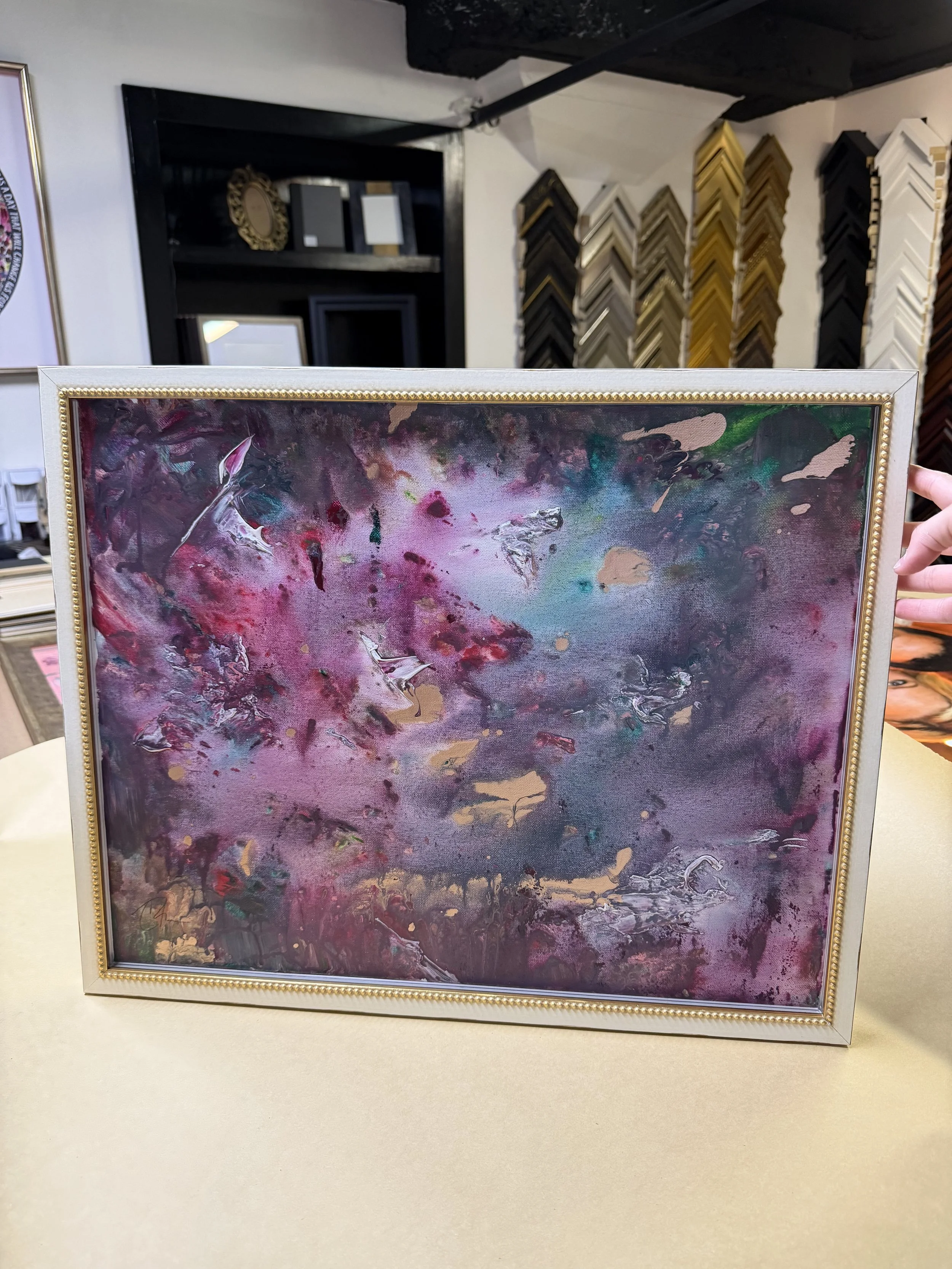 Abstract canvas painting held up in a cream and gold beaded frame inside the shop