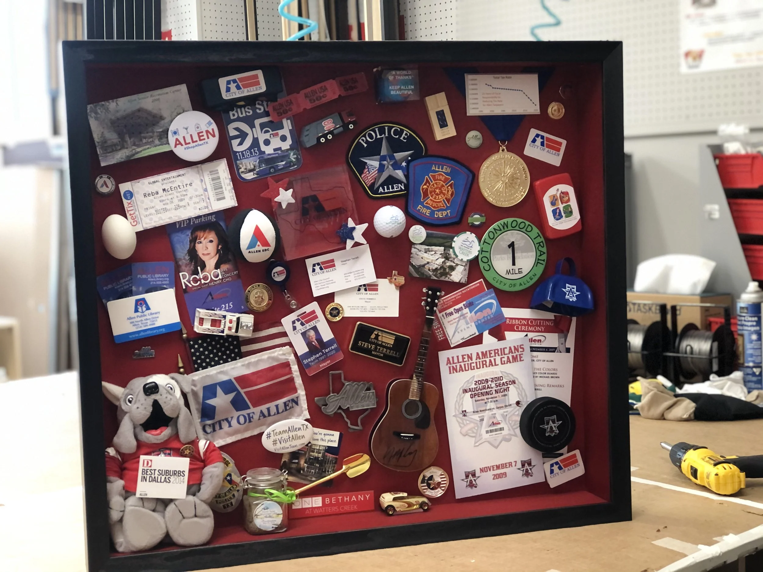Deep shadow box filled with city memorabilia, patches, tickets, and keepsakes on a red backing