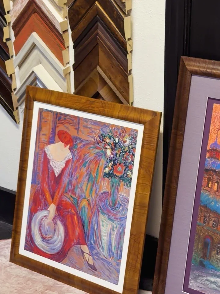 Framed fine-art prints beside a wall of wood moulding corner samples